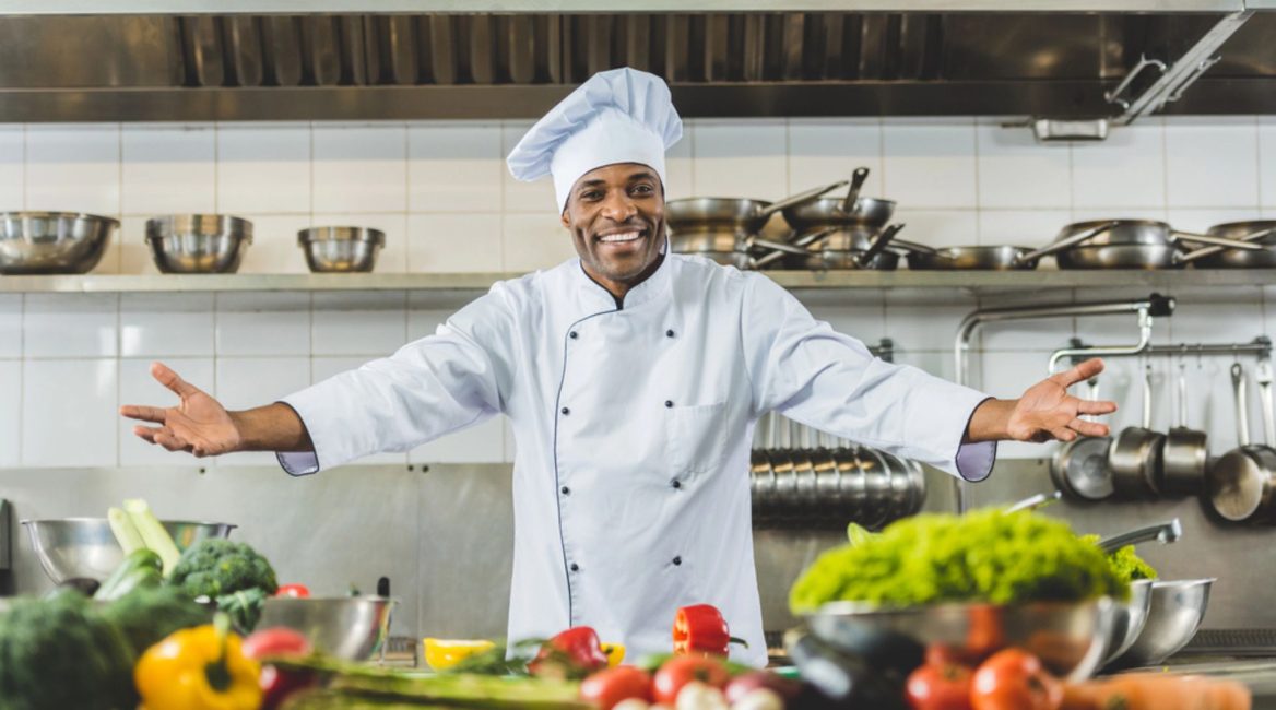 Chef souriant dans une cuisine professionnelle rénovée, entouré de légumes frais et d'équipements modernes