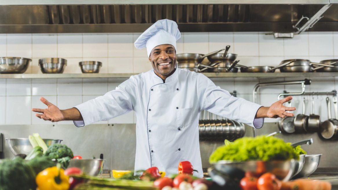 Chef souriant dans une cuisine professionnelle rénovée, entouré de légumes frais et d'équipements modernes