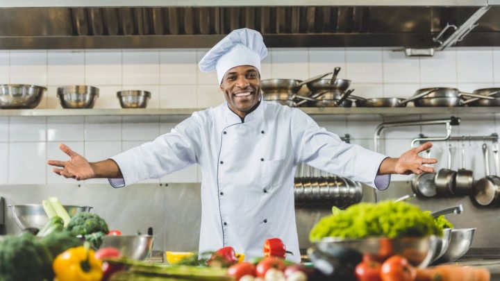 Chef souriant dans une cuisine professionnelle rénovée, entouré de légumes frais et d'équipements modernes