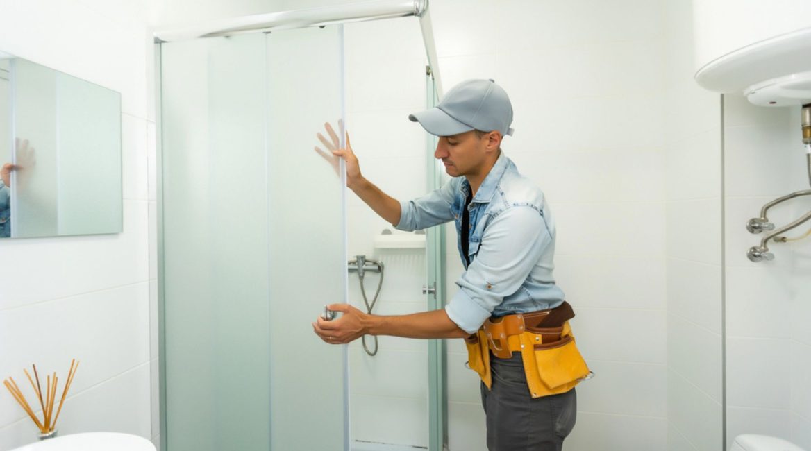 Artisan installant une paroi de douche dans le cadre de la rénovation d'une salle de bain professionnelle