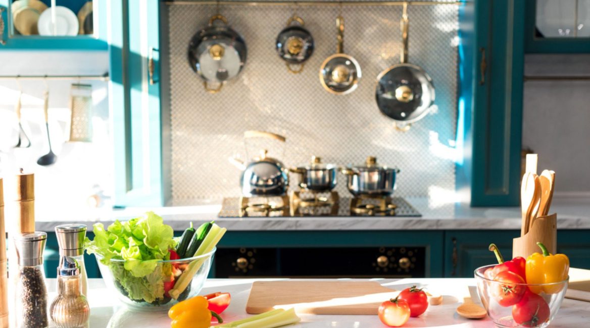 Cuisine lumineuse et professionnelle à domicile avec plan de travail en marbre, légumes frais, ustensiles de cuisine et casseroles suspendues.
