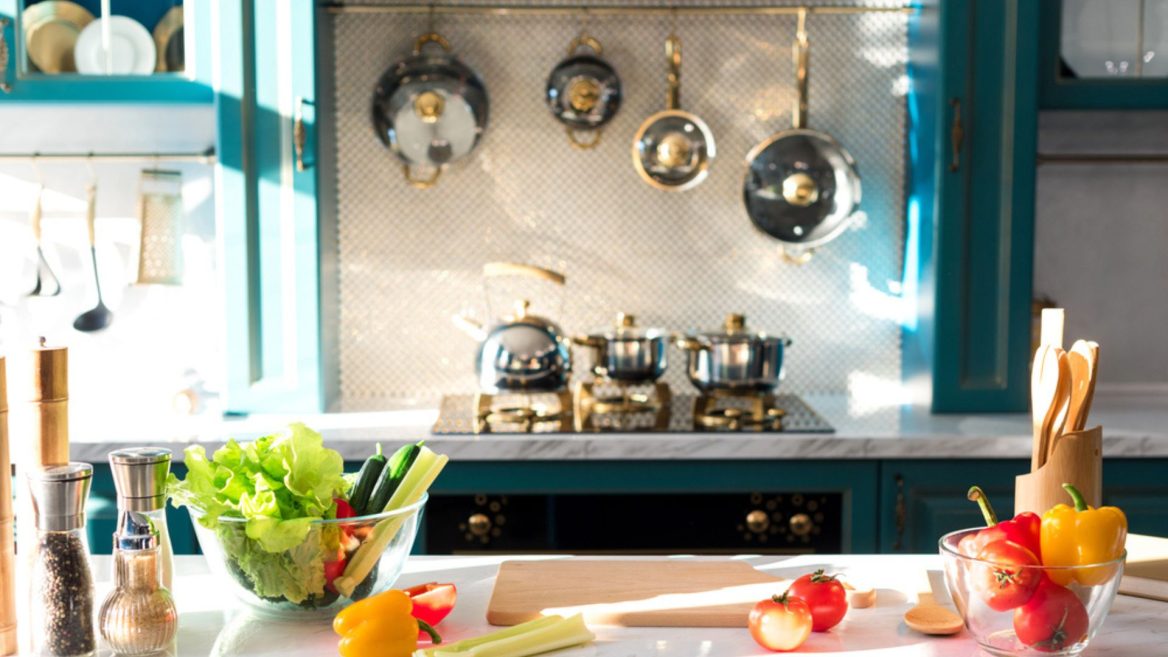 Cuisine lumineuse et professionnelle à domicile avec plan de travail en marbre, légumes frais, ustensiles de cuisine et casseroles suspendues.