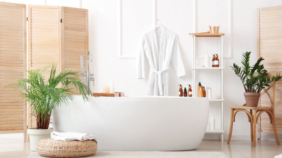 Salle de bain moderne et zen avec baignoire îlot blanche, plantes vertes, accessoires naturels et lumière douce, créant une ambiance spa apaisante.